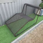 Brūns metāla šezlongs ar plašu sēdvietu pie metāla sienas