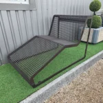 Brūns metāla šezlongs uz mākslīgā zāliena pie metāla sienas