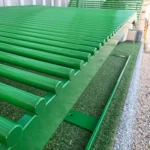 Zaļš metāla šezlongs pie industriālas ēkas fasādes.