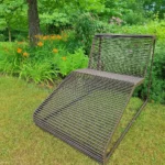 Brūns metāla dārza šezlongs zālienā pie puķu dobēm