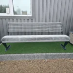 Metāla stienīšu sols frontāli pie industriālas ēkas