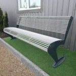 Metāla stienīšu sols no augšas pie ēkas uz mākslīgā zāliena