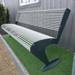 Metāla stienīšu sols pie ēkas fasādes ar dekoratīviem krūmiem