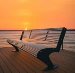 Metāla stienīšu sols uz terases pie ūdens saulrietā