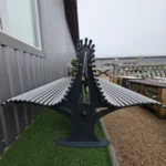 Garš sols ar metāla caurulītēm un plastmasas korķīšiem gar ēku