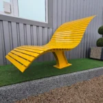 Dzeltenais metāla dizaina sols pie ēkas fasādes uz mākslīgā zāliena