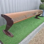 Metāla stienīšu sols pie industriālas ēkas uz mākslīgā zāliena