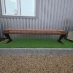 Garš metāla stienīšu sols frontāli pie ēkas fasādes