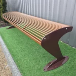 Metāla stienīšu sols ar metāla kājām pie zaļas apstādījumu zonas