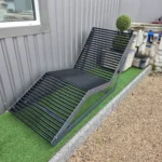 Metāla atpūtas sols pie ēkas uz mākslīgā zāliena